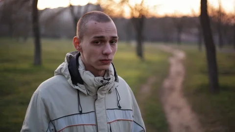 Handsome pensive young man with short hair looking at camera in the park in a Stock Footage 121062022
