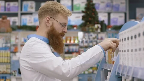 Handsome pharmacist standing in semi position near shelves while doing inventory Stock Footage 126527454
