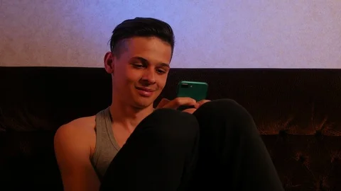 Handsome positive guy typing message on his phone on the sofa at home Video stock 106029108