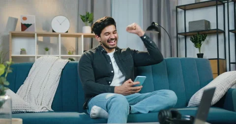 Handsome positive surprised young bearded guy sitting on the couch at home and Stock Footage 150157035