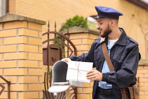 Handsome postman putting letters into mailbox on street Stock Photos