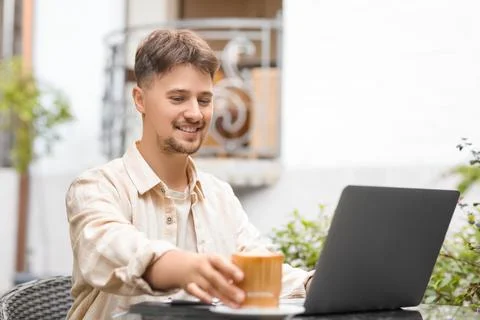 Handsome programmer with coffee and laptop working at table in street cafe Stock-Fotos