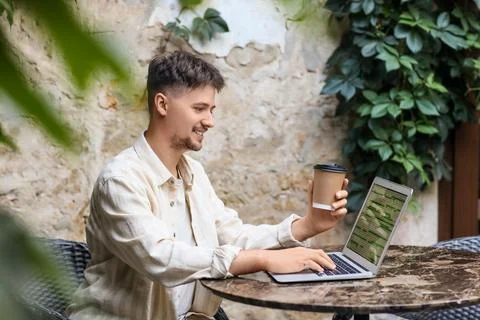 Handsome programmer with coffee and laptop working at table in street cafe Stock-Fotos
