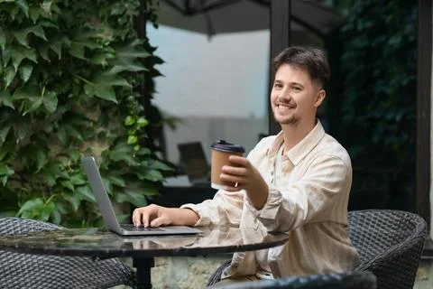Handsome programmer with coffee and laptop working at table in street cafe Stock-Fotos