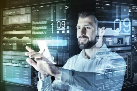 Handsome programmer holding a smartphone and looking at the screen of computer Stock Photos