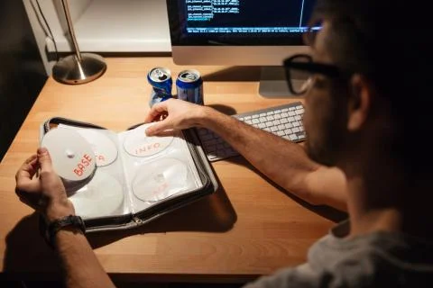 Handsome programmer using computer and choosing CD with data Stock Photos