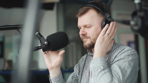Handsome radio host is preparing to broadcast on a radio show and puts on headph Vidéo 240755003
