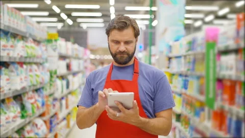 Handsome salesman using digital tablet standing among shelves In supermarket Stock Footage 92208191