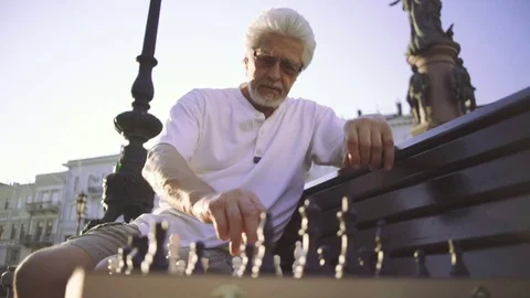 Handsome senior man playing chess outdoors in city, slow motion Stock Footage 78485423