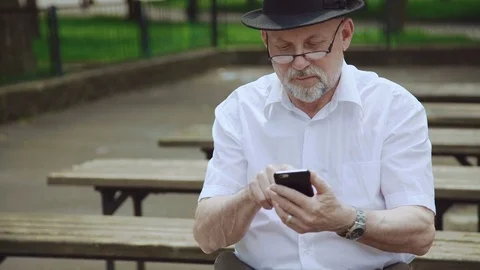 Handsome senior man using the smartphone on the bench in park 4K Video stock 76925094