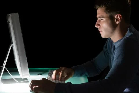 Handsome serious computer engineer looking at computer at night Stock Photos