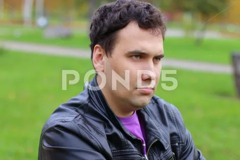 Handsome serious man in leather jacket looks at away in park at summer Stock Photos
