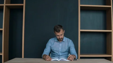 Handsome sitting down by the table and starts reading a book Stock Footage 95919360
