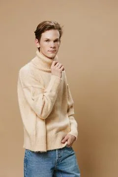 A handsome, slender guy in a long oversized beige sweater straightens his Stock Photos