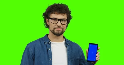 Handsome smiled young man posing with a black smartphone in hands and pointing Stock Footage 90710970