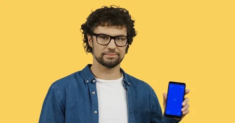 Handsome smiled young man posing with a black smartphone in hands and pointing Stock-Footage 104229961