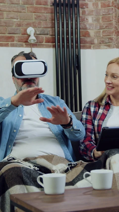 Handsome smiling bearded man in augmented reality goggles sitting together with  Stock Footage 329676371