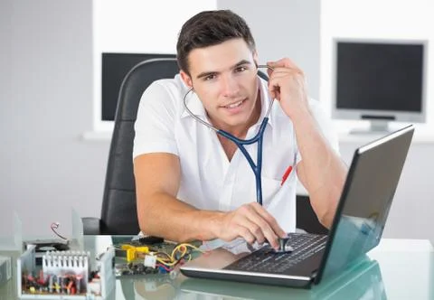 Handsome smiling computer engineer examining laptop with stethoscope Stock Photos