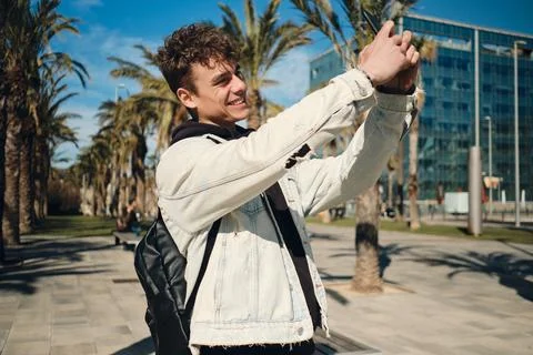 Handsome smiling guy with backpack happily taking photo on smartphone on city Stock Photos