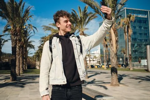 Handsome smiling guy happily taking selfie on smartphone in park. Young stylish Stock Photos