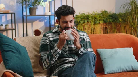 Handsome smiling indian man drinking a cup of coffee or herbal tea sitting at Stock Footage 233942470