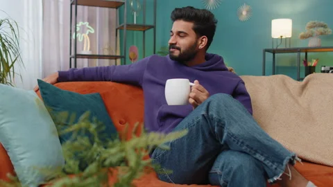 Handsome smiling indian man drinking a cup of coffee or herbal tea sitting at Stock Footage 237350789