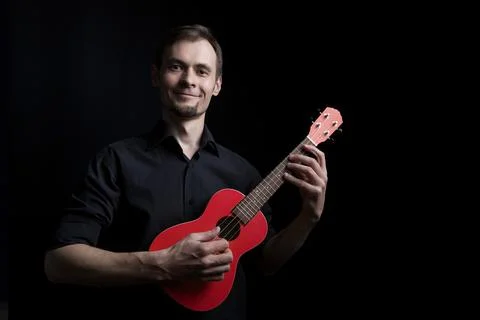 Handsome smiling low key man portrait playing on fun red ukulele guitar over Stock Photos