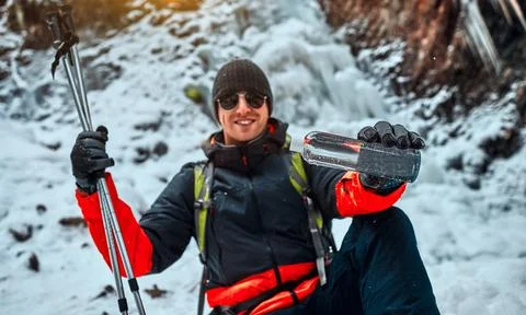 Handsome smiling man in assorted warm winter clothes and gloves holds a bottl Stock Photos