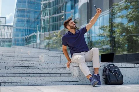 Handsome smiling man in casual clothes making selfie sitting on background of Stock Photos