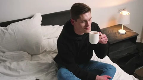 Handsome smiling Man drinking coffee sitting in bed. Man drinking coffee resting Stock Footage 148385652