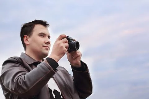 Handsome smiling man in leather jacket holds camera against sky Stock Photos