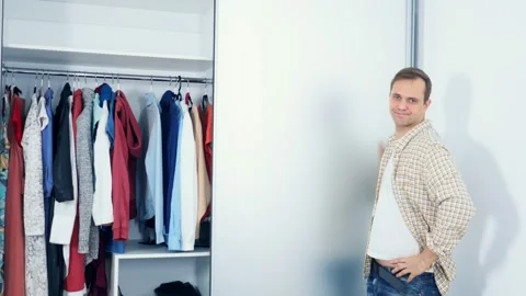 Handsome smiling man opens wardrobe with clothes, copy space Stock Footage 147984845