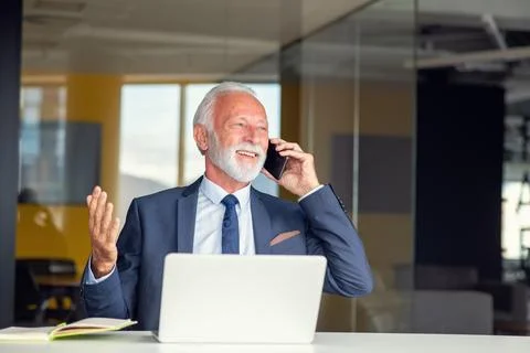 Handsome smiling senior man while sitting at his cozy workplace with laptop at Stock Photos