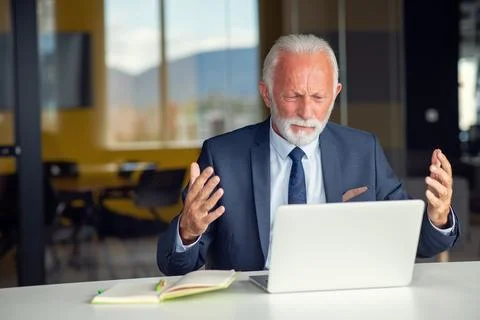 Handsome smiling senior man while sitting at his cozy workplace with laptop at Фото