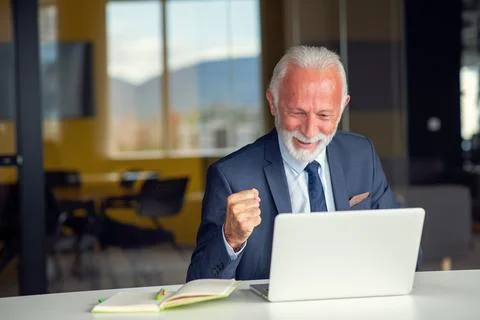 Handsome smiling senior man while sitting at his cozy workplace with laptop at Foto stock