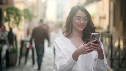 Handsome smiling woman in glasses with mobile phone walking on the street Stock Footage 197141553