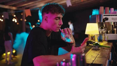 Handsome sociable boy using smartphone checking news drinking alcohol cocktail Stock Footage 115366344