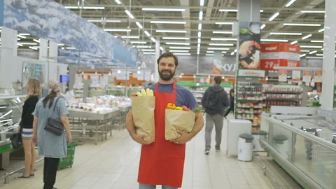 Handsome store employee in red aport with grocery paper bags standing in Stock Footage 92546659