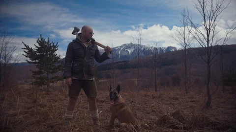 Handsome strong lumberjack holding axe in forest and enjoying with his dog Stock Footage 87566196