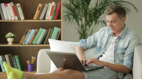 Handsome student sitting on couch and using laptop Stock Footage 27692050