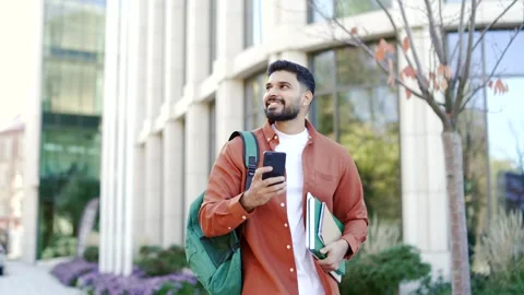 Handsome student uses a mobile phone while walking in campus near university Stock Footage 304590677