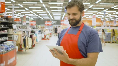 Handsome supermarket clerk with beard using a touch screen tablet in supermarket Stock Footage 92213532