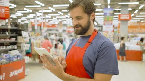 Handsome supermarket clerk using a touch screen tablet in supermarket, he is Stock Footage 92298342