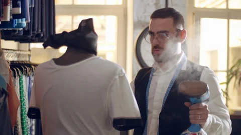 Handsome tailor stroking tshirt with a vertical steam iron at fashion saloon. Stock Footage 109329058