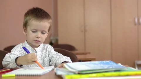 A handsome three year old boy sits at his desk in the class and thinks about the Stock Footage 140009845