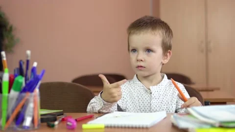A handsome three year old boy sits at his desk in the class and thinks about the Stock Footage 140053002