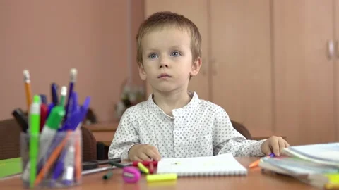A handsome three year old boy sits at his desk in the class and thinks about the 库存影片 140220790
