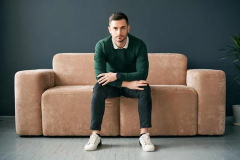 Handsome trendy man posing looking to camera while sitting on comfort sofa in Foto stock