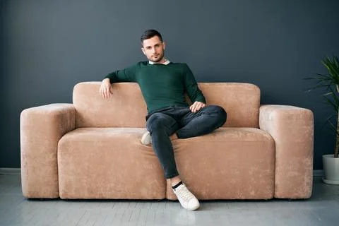 Handsome trendy man posing looking to camera while sitting on comfort sofa in Foto stock