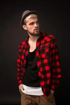 Handsome trendy young guy at the studio on black background. He wears beard and Stock Photos